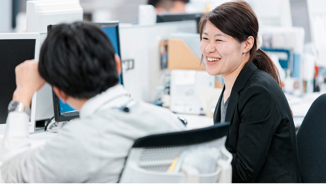 和田 里香がオフィスで同僚と笑顔で会話をしている姿