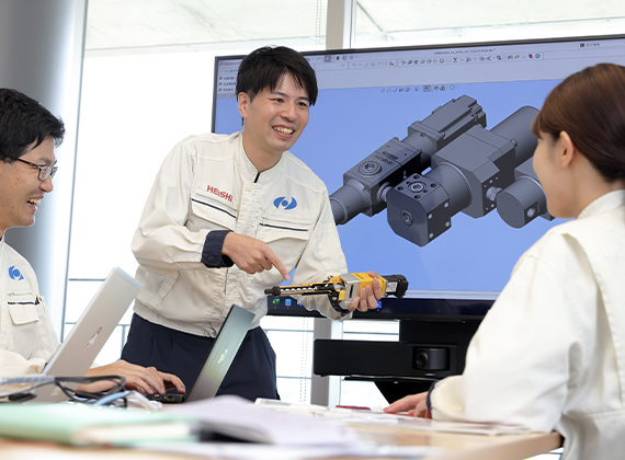 オフィスで同僚と話しながら仕事に励む様子